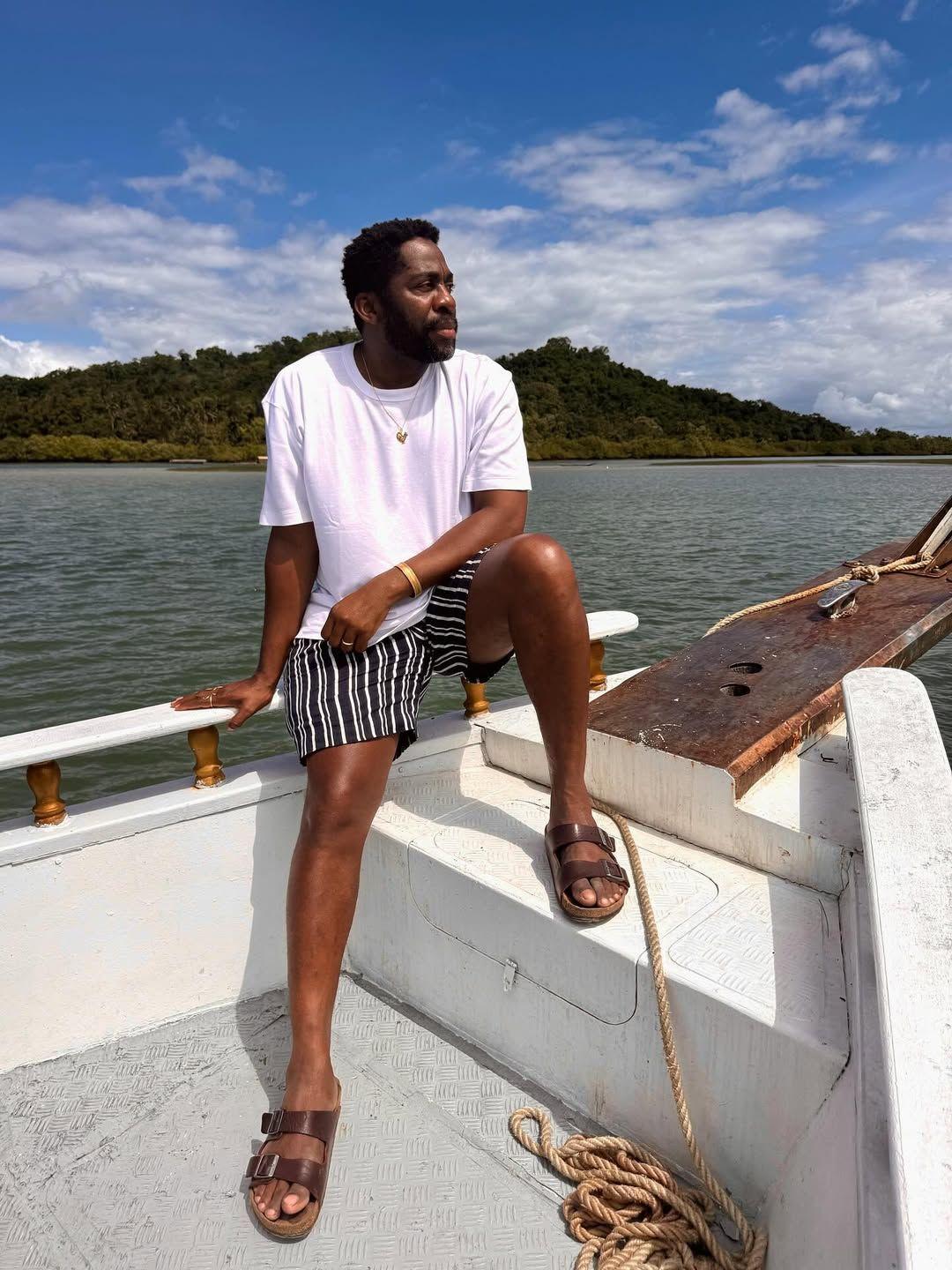 Lázaro Ramos sentado e olhando para o lado em uma praia.