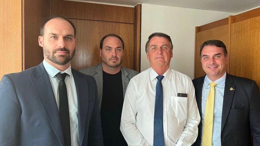 Jair, Eduardo, Carlos e Flávio Bolsonaro posam lado a lado em uma sala com painéis de madeira; três deles usam terno e gravata, enquanto um veste blazer e camiseta. Todos olham diretamente para a câmera. Imagem usada em matéria sobre filhos defenderem André Fernandes após declarações de Michelle.
