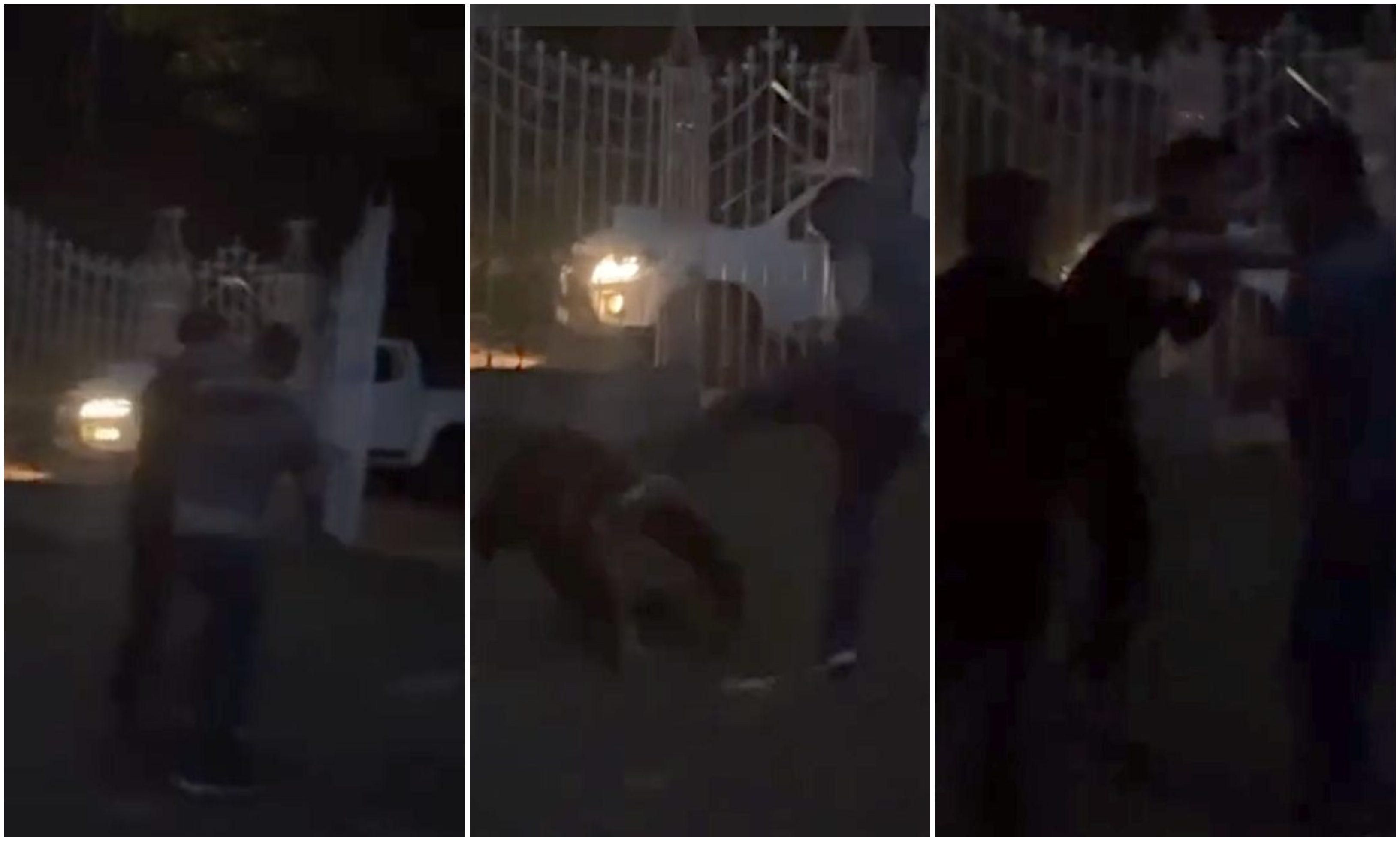 Três quadros mostram uma briga noturna em frente a um portão de grades metálicas, com um carro branco iluminado ao fundo. No primeiro quadro, duas pessoas parecem se aproximar ou discutir. No segundo, uma pessoa no chão é chutada por outra. No terceiro, duas pessoas continuam trocando golpes enquanto uma terceira tenta intervir.