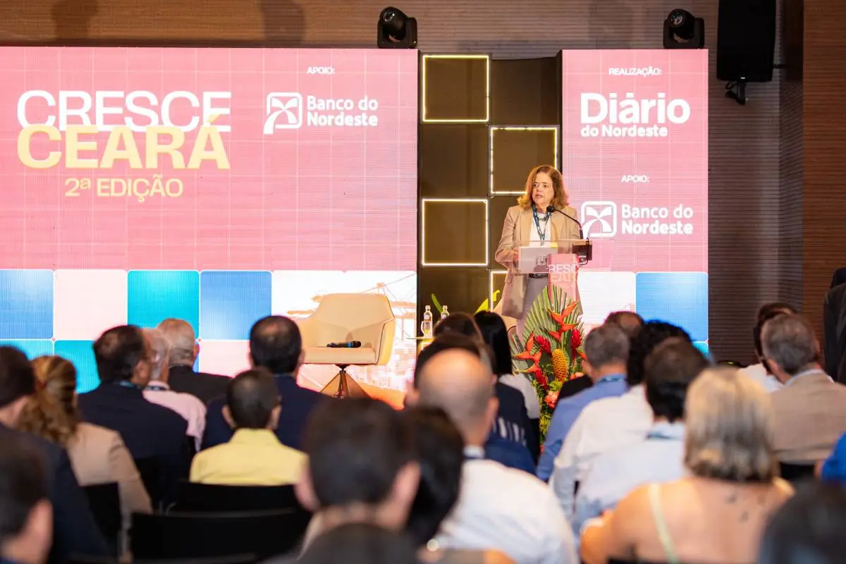 Painel de discussão em um auditório com pessoas sentadas em poltronas brancas sobre um palco, diante de um grande telão vermelho com a frase “Cresce Ceará”.