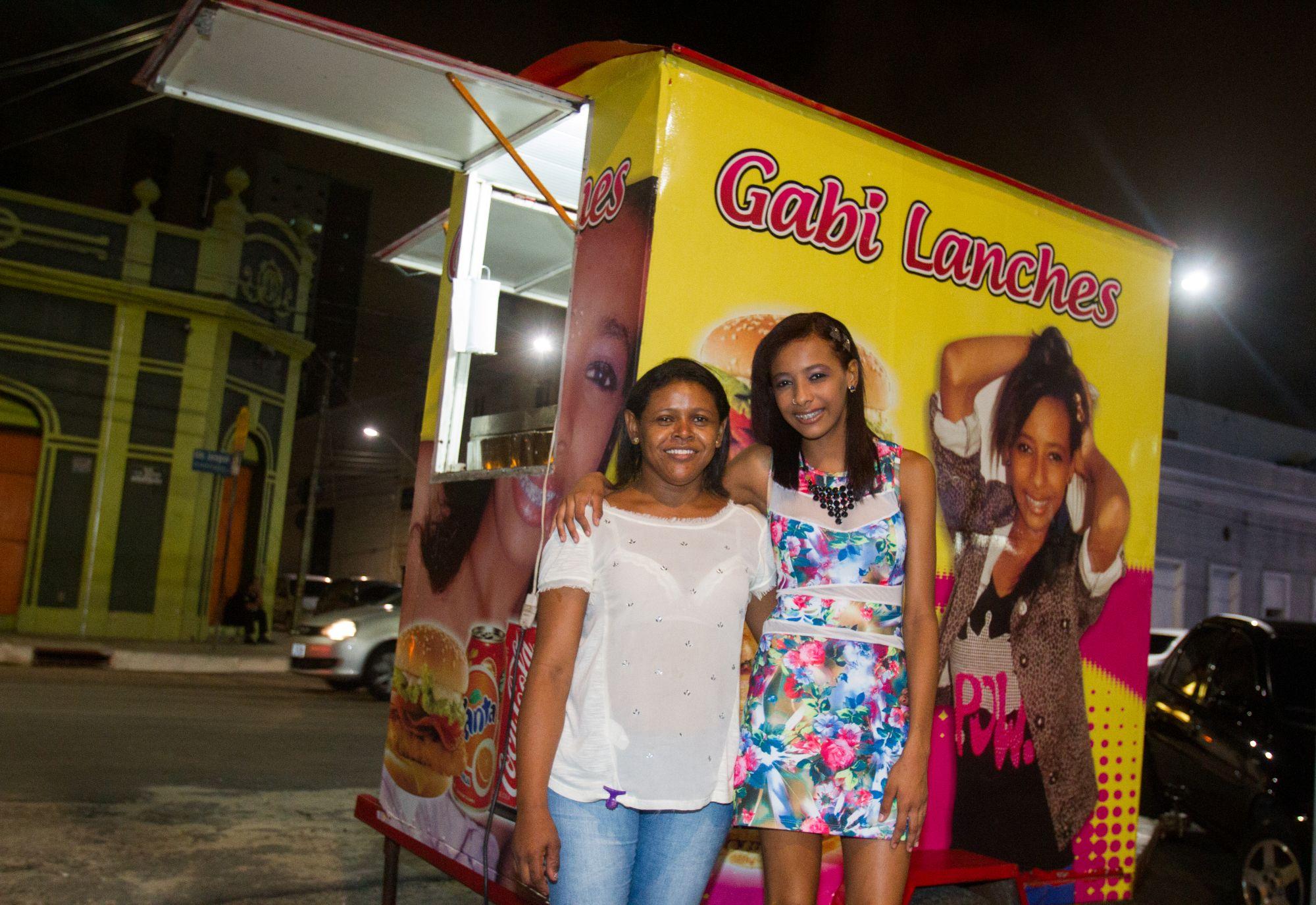 Mulheres ao lado do seu food truck Gabi Lanches decorado com imagens de hambúrgueres e lanches.