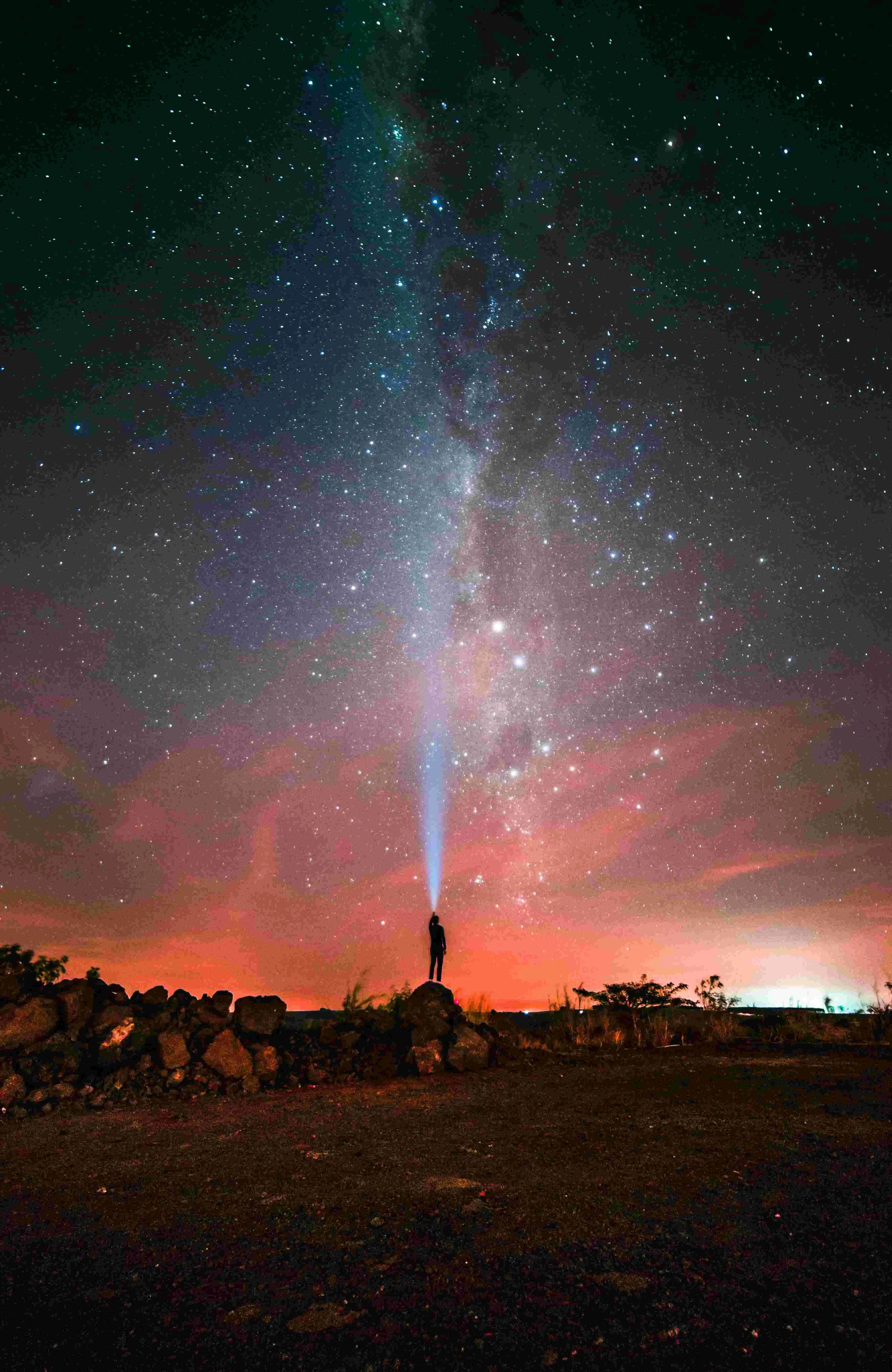 Uma figura humana com uma luz direcionada para cima sob um majestoso céu noturno repleto de estrelas e a faixa brilhante da Via Láctea.