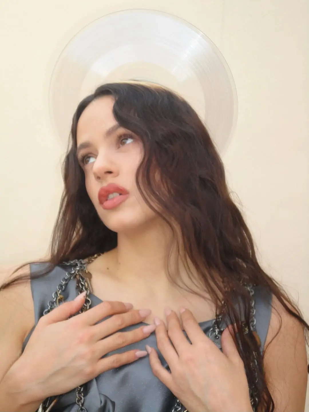 Cantora Rosalía posando com as mãos sobre o peito, cabelo escuro ondulado e um halo de vinil translúcido.