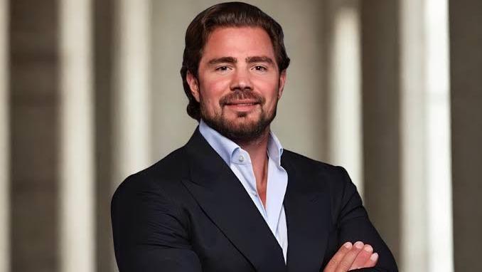 Daniel Vorcaro é um homem de meia idade, de barba bem feita e cabelo bem penteado para trás. Na foto, ele está de terno preto e camisa social azul, de braços cruzados.