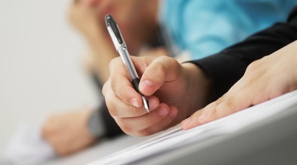 Mão segura caneta enquanto escreve em papel.