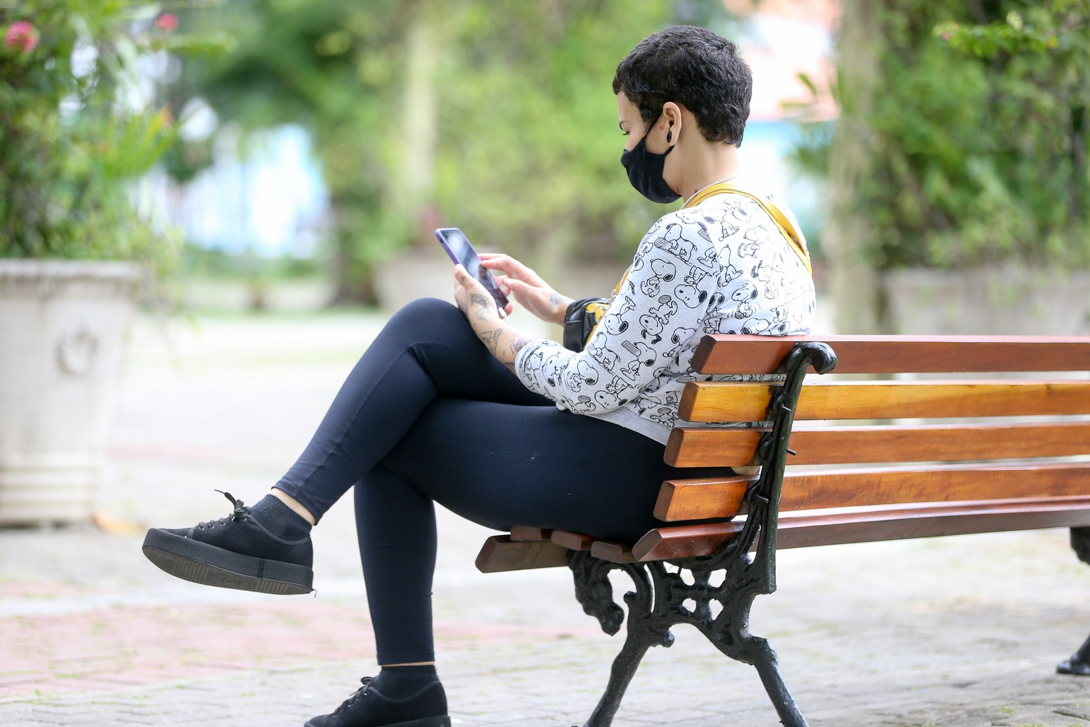 Foto que contém mulher sentada em praça com um celular nas mãos.