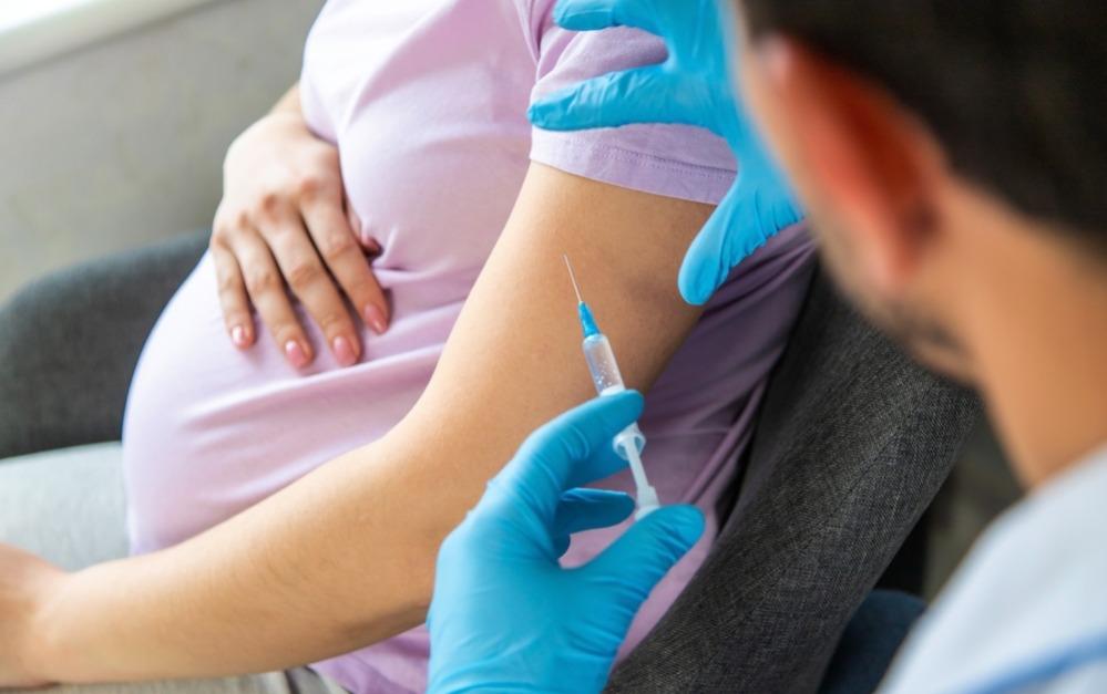 Mulher grávida toma vacina em posto de saúde.