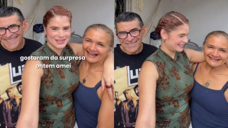 Jovem mulher sorri ao lado dos pais visivelmente emocionados, após presenteá-los com um apartamento.