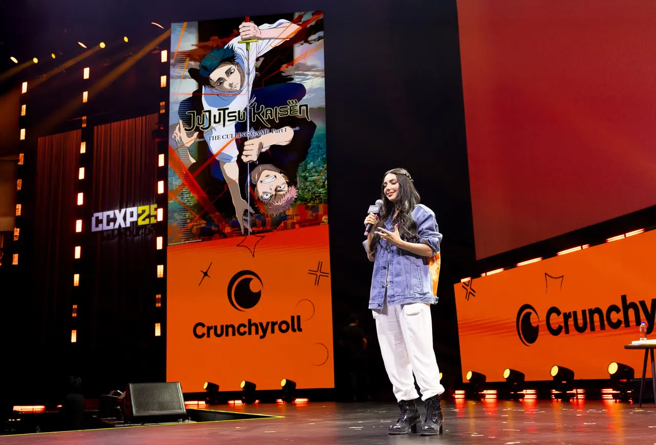 Nyvi Estephan vestindo jaqueta jeans no palco Thunder da CCXP ao lado de telão com foto de Jujutsu Kaisen.