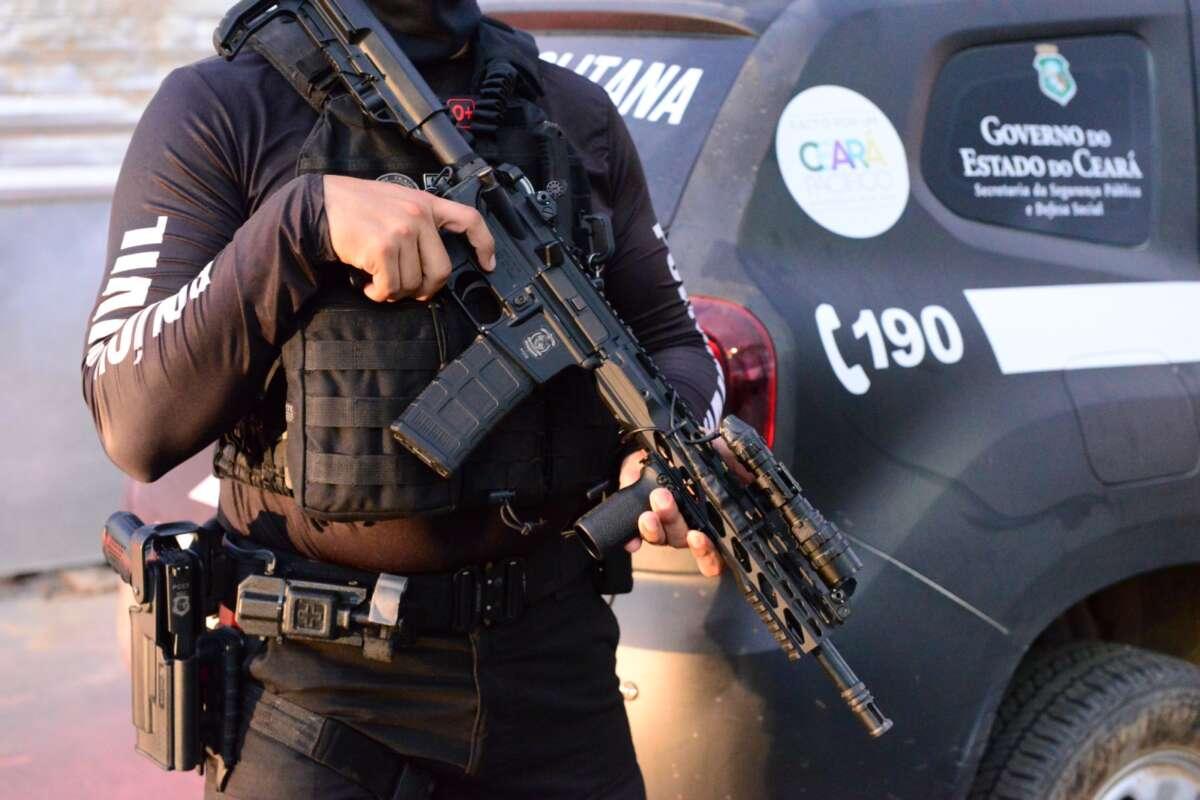 Policial segura arma. Imagem mostra apenas braços e mãos segurando a arma.