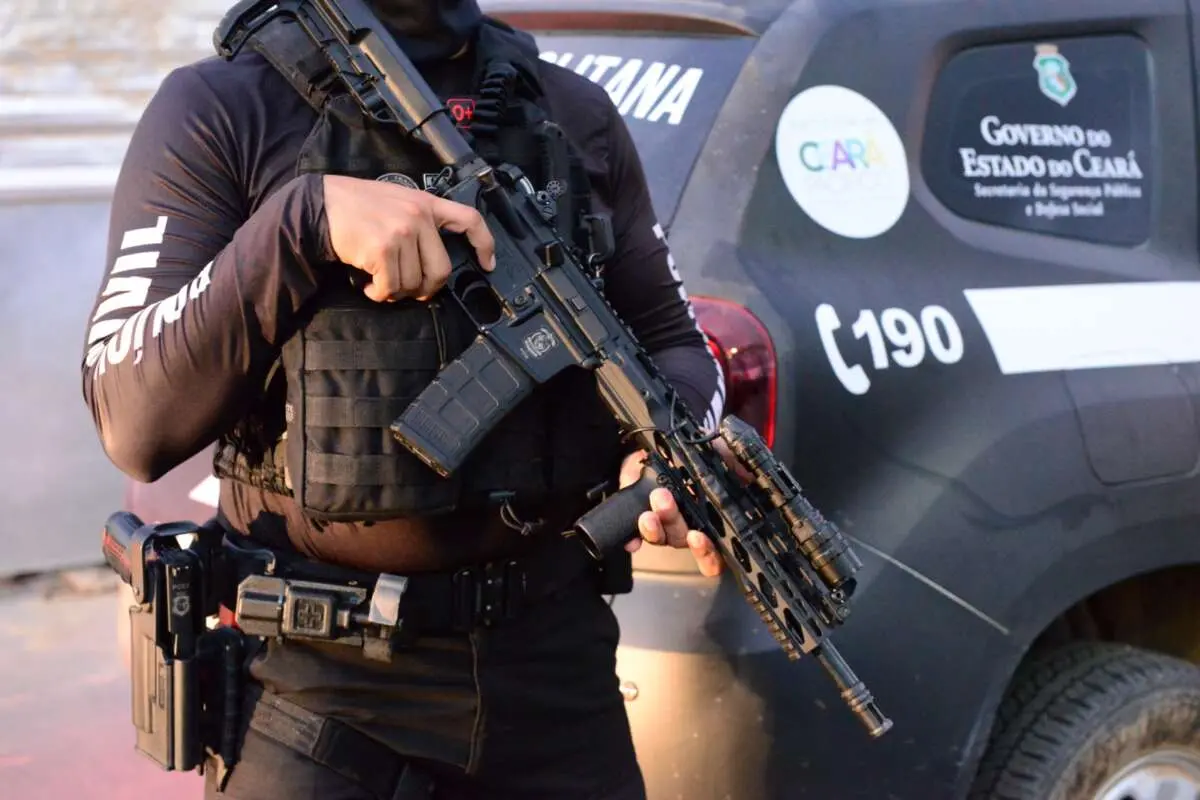 Policial segura arma. Imagem mostra apenas braços e mãos segurando a arma.