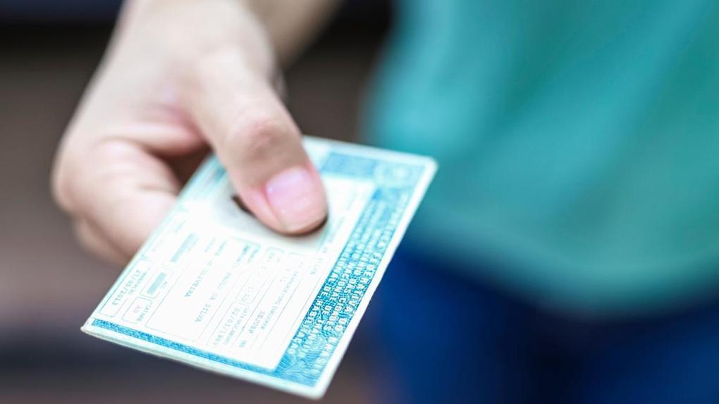 Imagem mostra mão de pessoa entregando ou mostrando uma Carteira Nacional de Habilitação (CNH) brasileira.