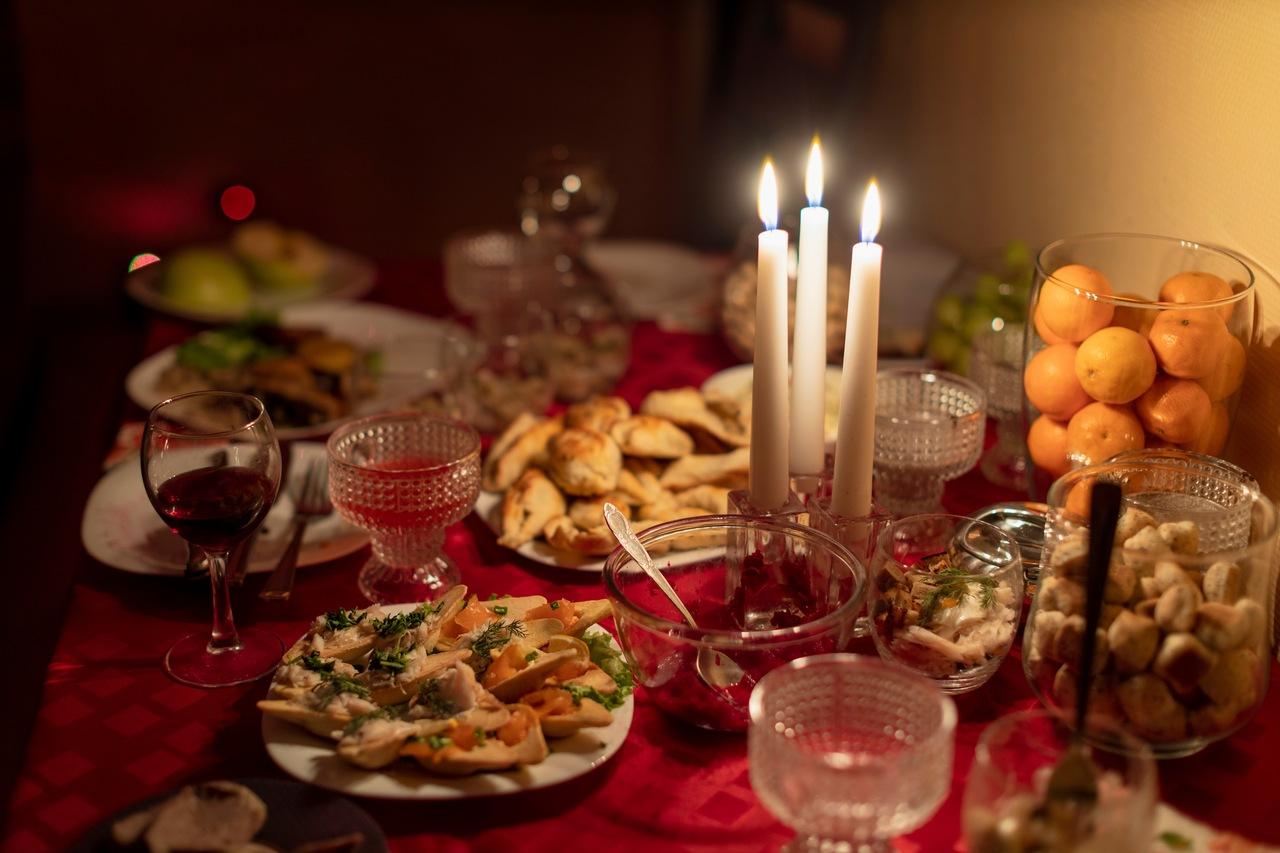 Mesa de toalha vermelha repleta de variados pratos de comida e taças de vinho. Ao centro, três velas.