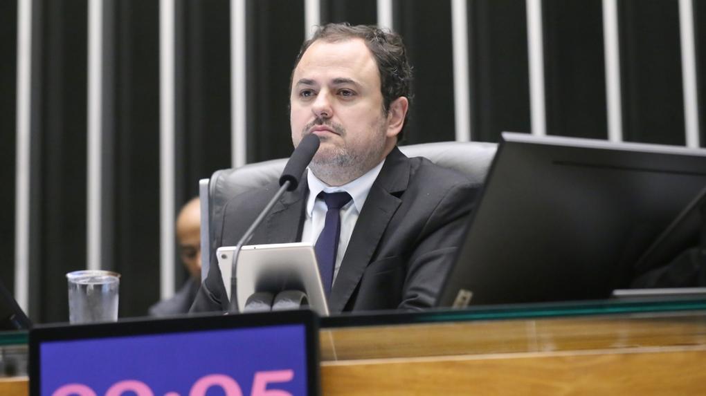 O deputado Glauber Braga é um homem de meia-idade, branco e de barba rala, grisalha e cabelo preto. Na foto, ele está sério e usa terno cinza com camisa social branca e gravata azul.