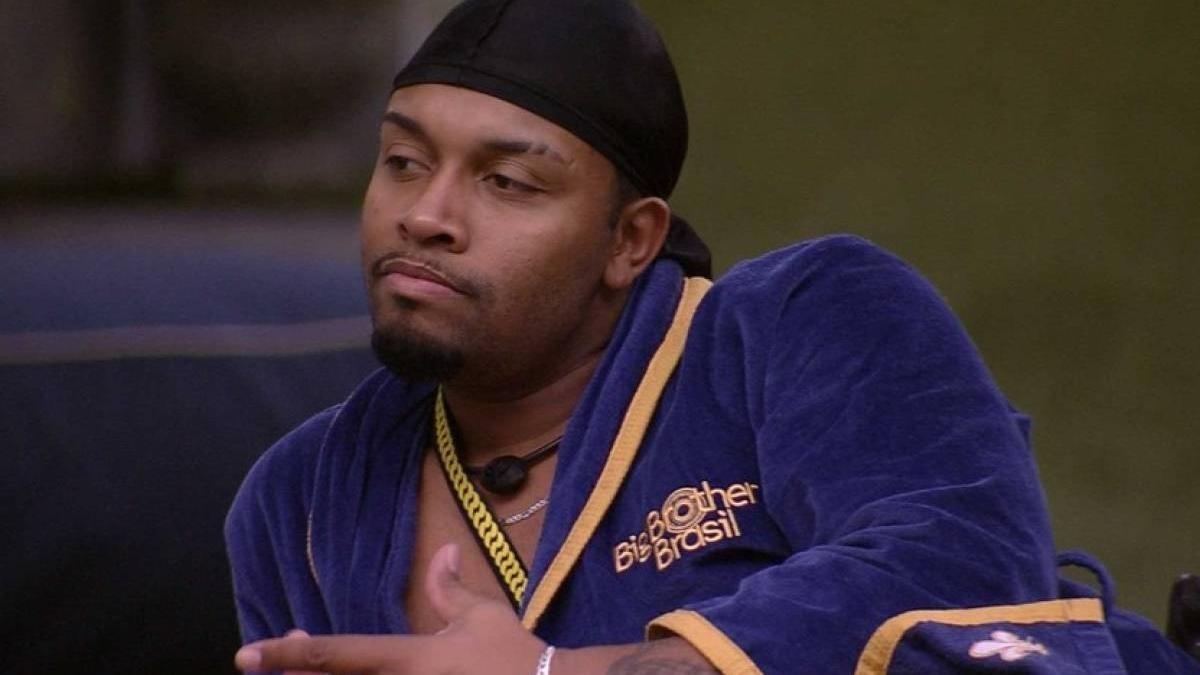 Nego Di é um homem jovem, negro e de cavanhaque. Na foto, ele usa o roupão de líder do BBB e um lenço no cabelo.