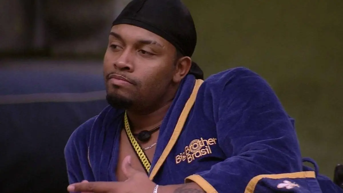 Nego Di é um homem jovem, negro e de cavanhaque. Na foto, ele usa o roupão de líder do BBB e um lenço no cabelo.