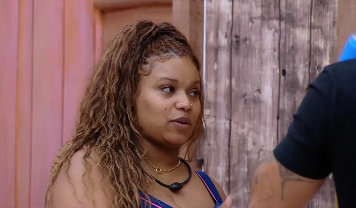 Camilla é uma mulher negra, jovem, de cabelo castanho longo e trançado. Na foto, ela está dialogando com alguém.