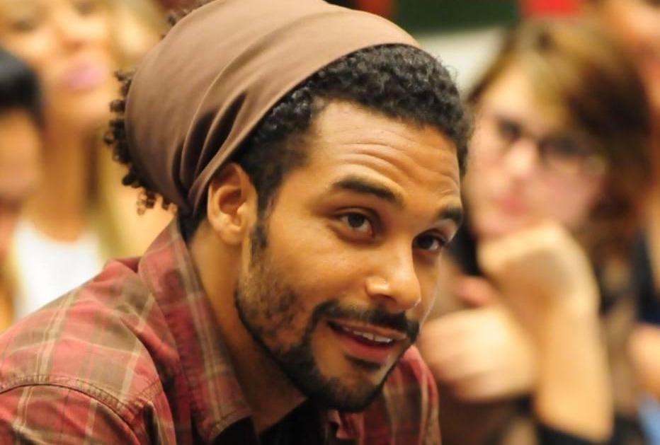 Daniel é um homem jovem, negro e de cabelo preso em um lenço. Na foto, ele está sorrindo.