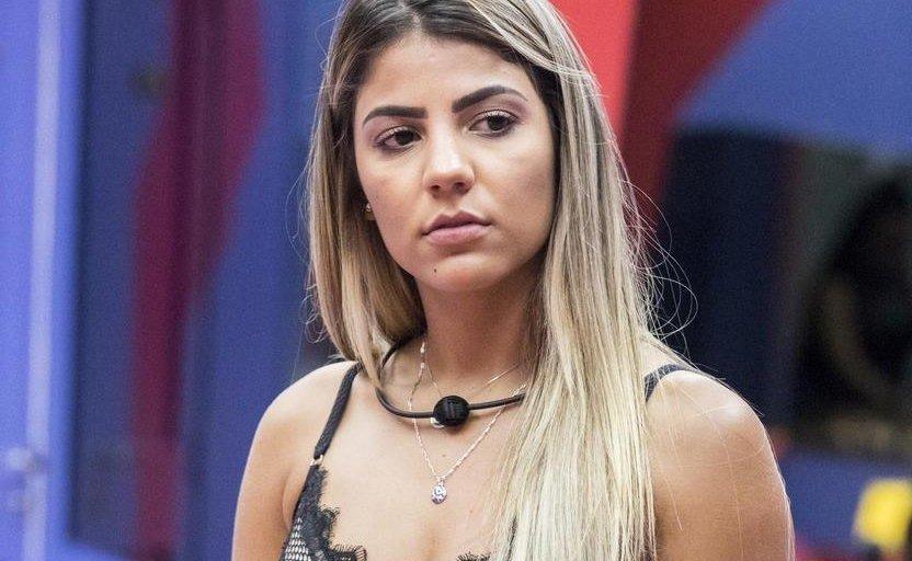 Hariany é uma mulher jovem branca e loira de cabelo longo e liso. Na foto, ela está olhando de lado, desconfiada.