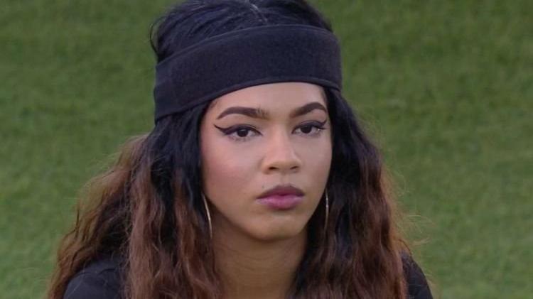 Maria é uma mulher jovem negra de cabelo longo e ondulado. Na foto, ela está com expressão séria.