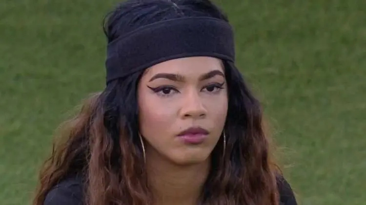 Maria é uma mulher jovem negra de cabelo longo e ondulado. Na foto, ela está com expressão séria.