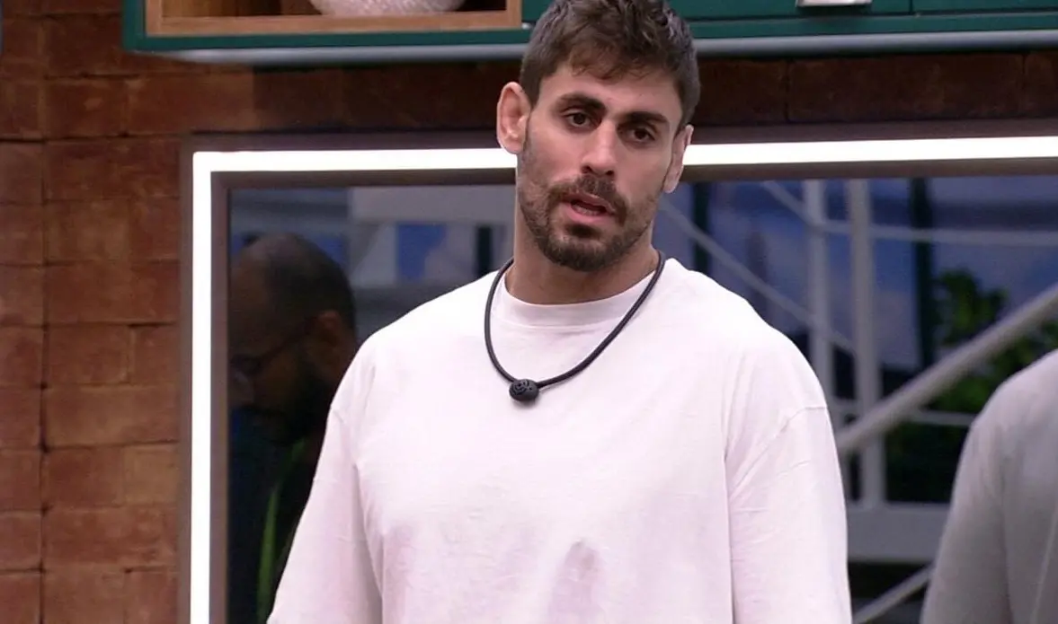 Cara de Sapato é um homem branco de cabelo preto e barba preta. Na foto, ele está com uma camisa moletom branca, enquanto conversa com alguém.