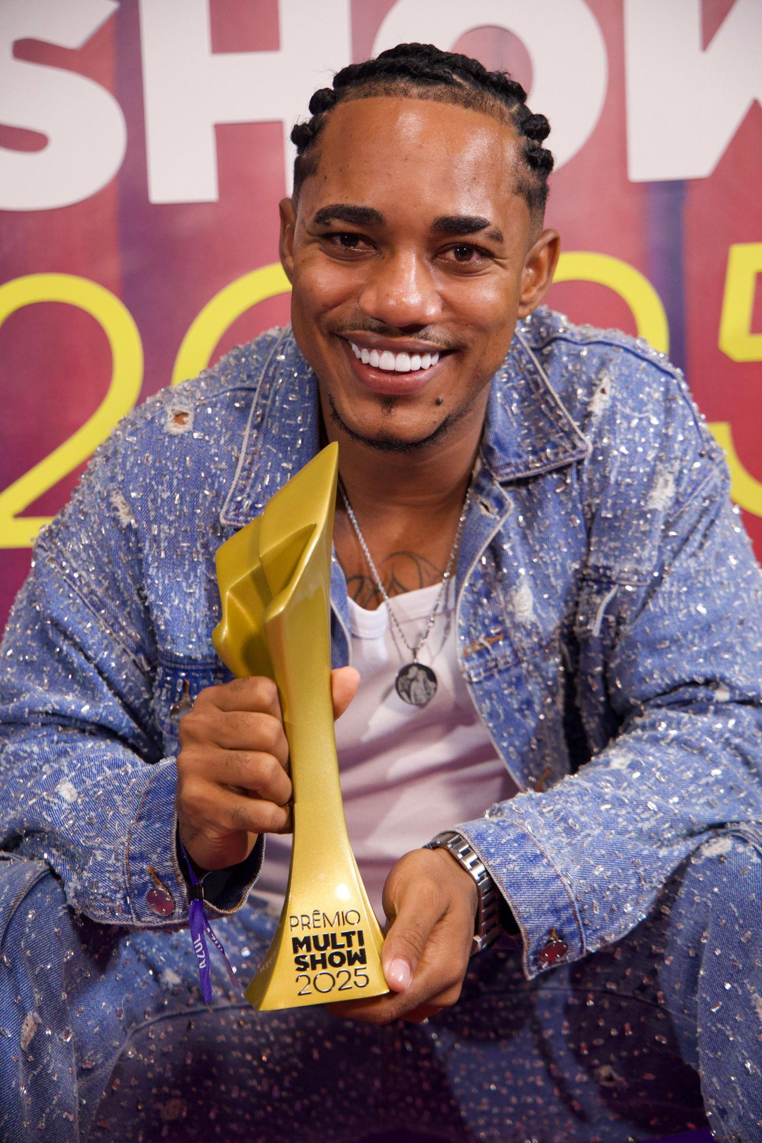 cantor o kanalha exibindo prêmio multishow. ele exibe colar com foto de preta gil.