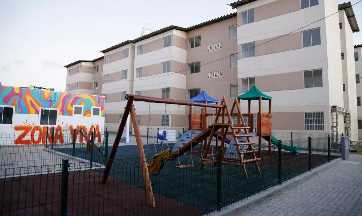 Imagem de um complexo residencial com prédios de apartamentos e um playground infantil equipado com balanços e escorregador, ilustrando construção civil e financiamento imobiliário.