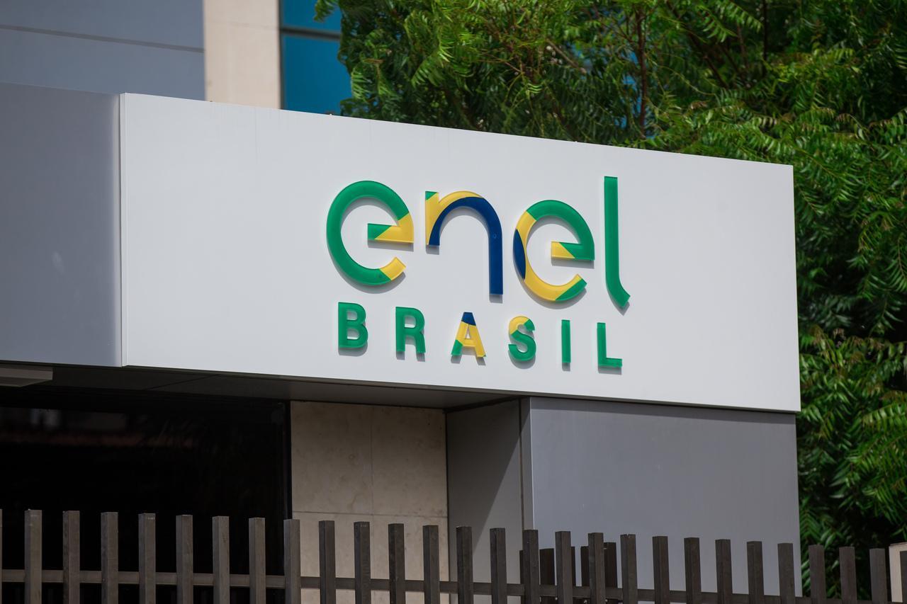 Logotipo da Enel Brasil em fachada corporativa, com letras estilizadas nas cores verde, azul e amarelo, representando a empresa de energia elétrica no Brasil.