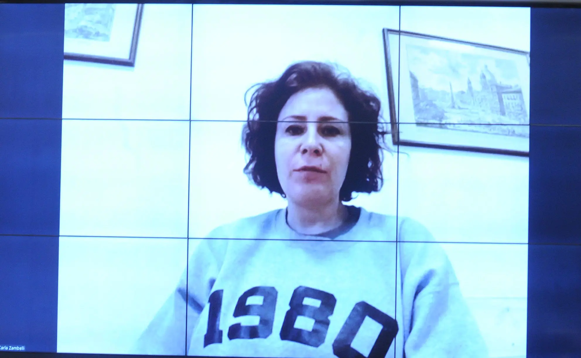 deputada carla zambelli fotografada aparecendo em um telão. ela veste blusa branca, com os números 1980 escritos em letra preta.