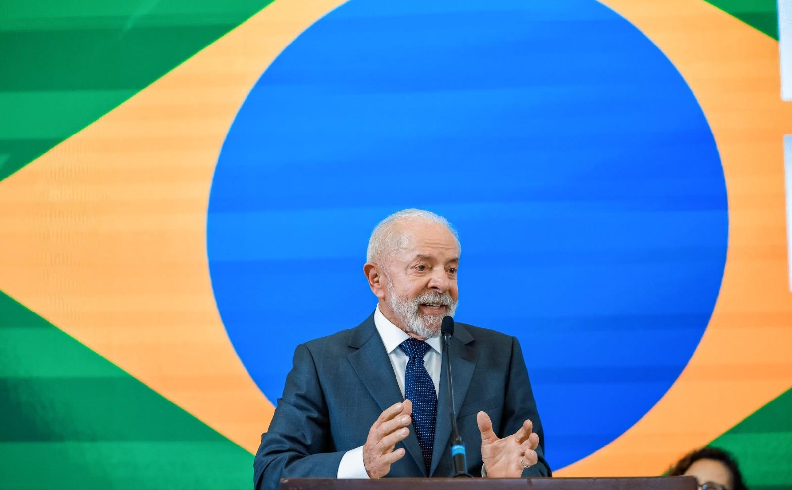 Lula discursa durante evento oficial. Atrás dele há uma bandeira gigante do Brasil.