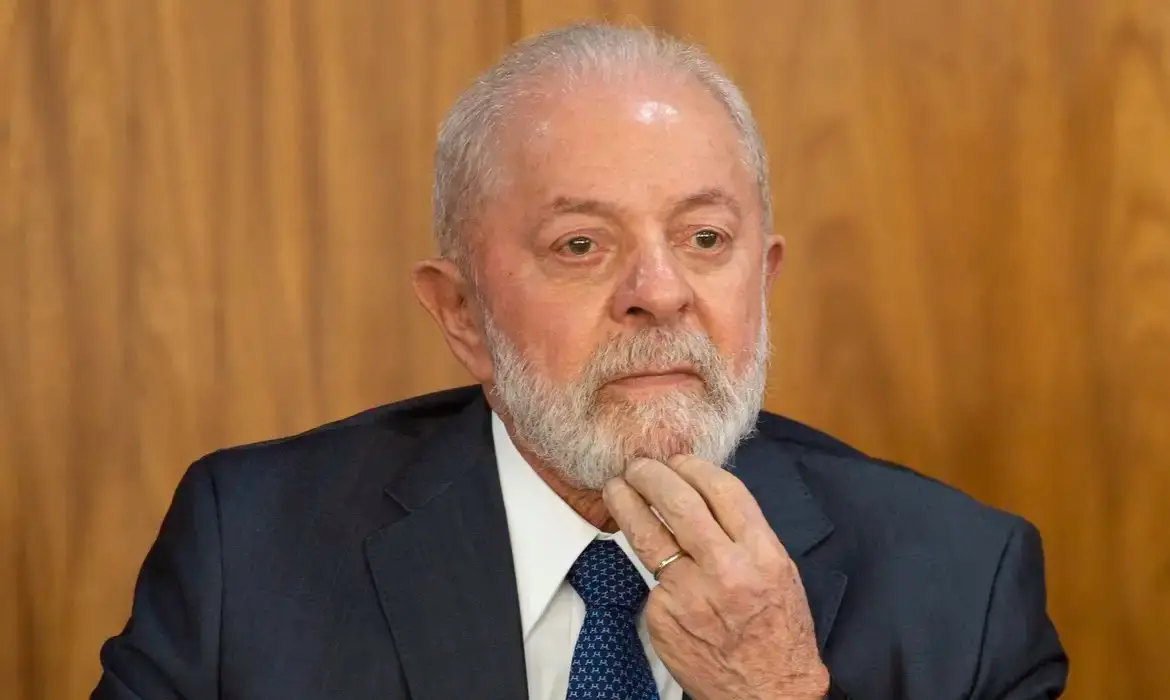 Luiz Inácio Lula da Silva, Presidente do Brasil, com expressão séria e reflexiva, tocando o queixo.