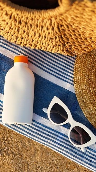 Protetor solar, óculos escuros e chapéus de palha sobre areia da praia.