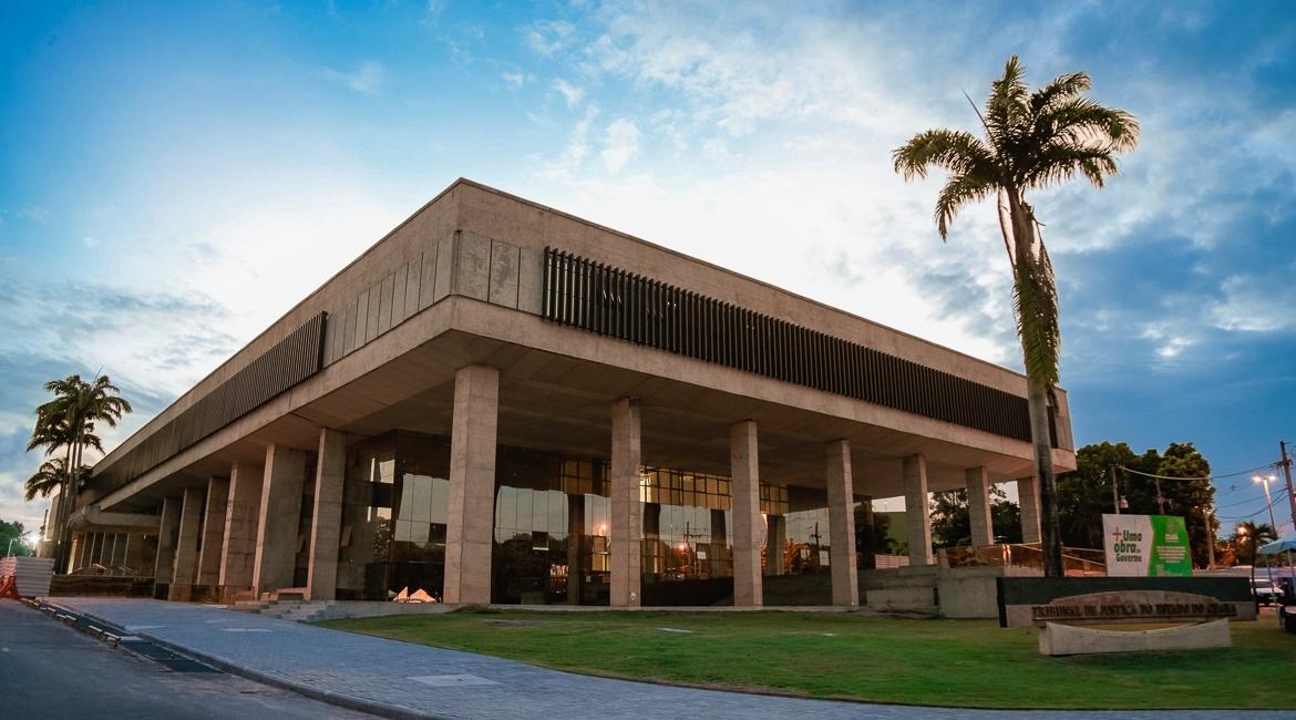 Imagem de um edifício moderno com arquitetura contemporânea, cercado por palmeiras e um céu parcialmente nublado, ideal para negócios e eventos.