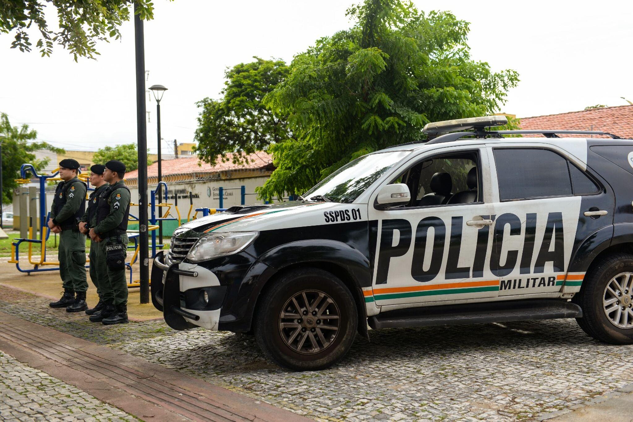 Três policiais militares ao lado de uma viatura.