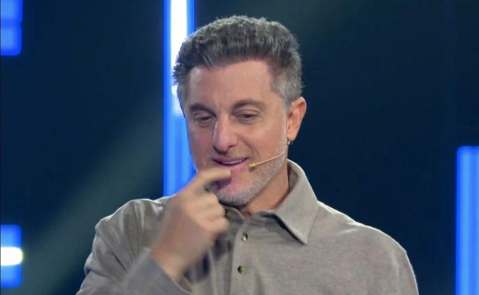 Luciano Huck com a mão no queixo, com expressão de dúvida.