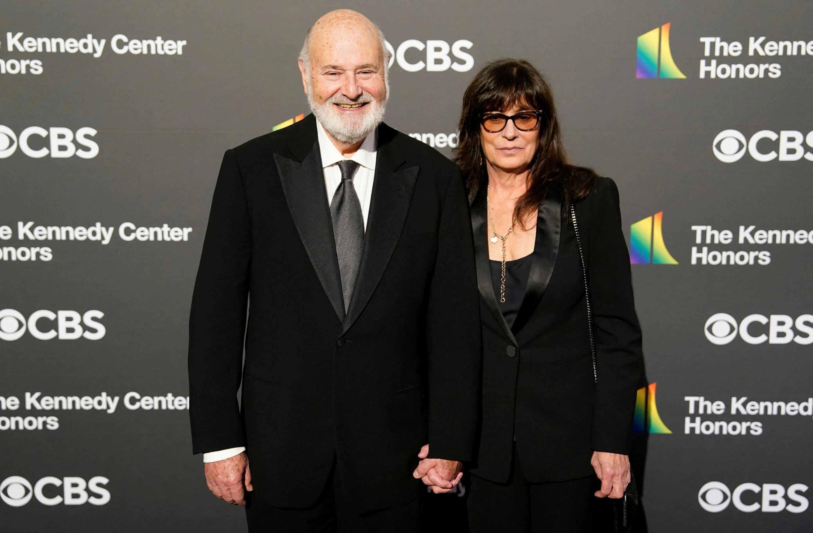 Rob Reiner e a esposa Michele diante de um painel com a marca da emissora CBS. eles vestem roupas pretas.