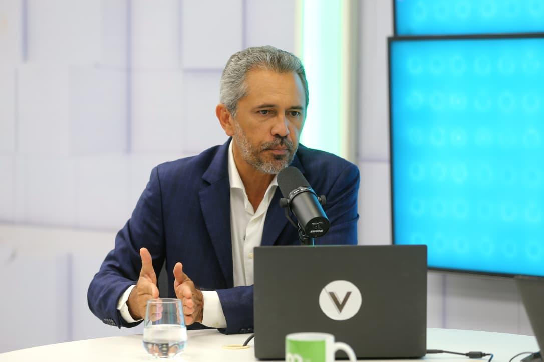 A imagem mostra o governador do Ceará Elmano de Freitas, sentado, com as mãos em cima da mesa, durante entrevista, em um estúdio do Sistema Verdes Mares.