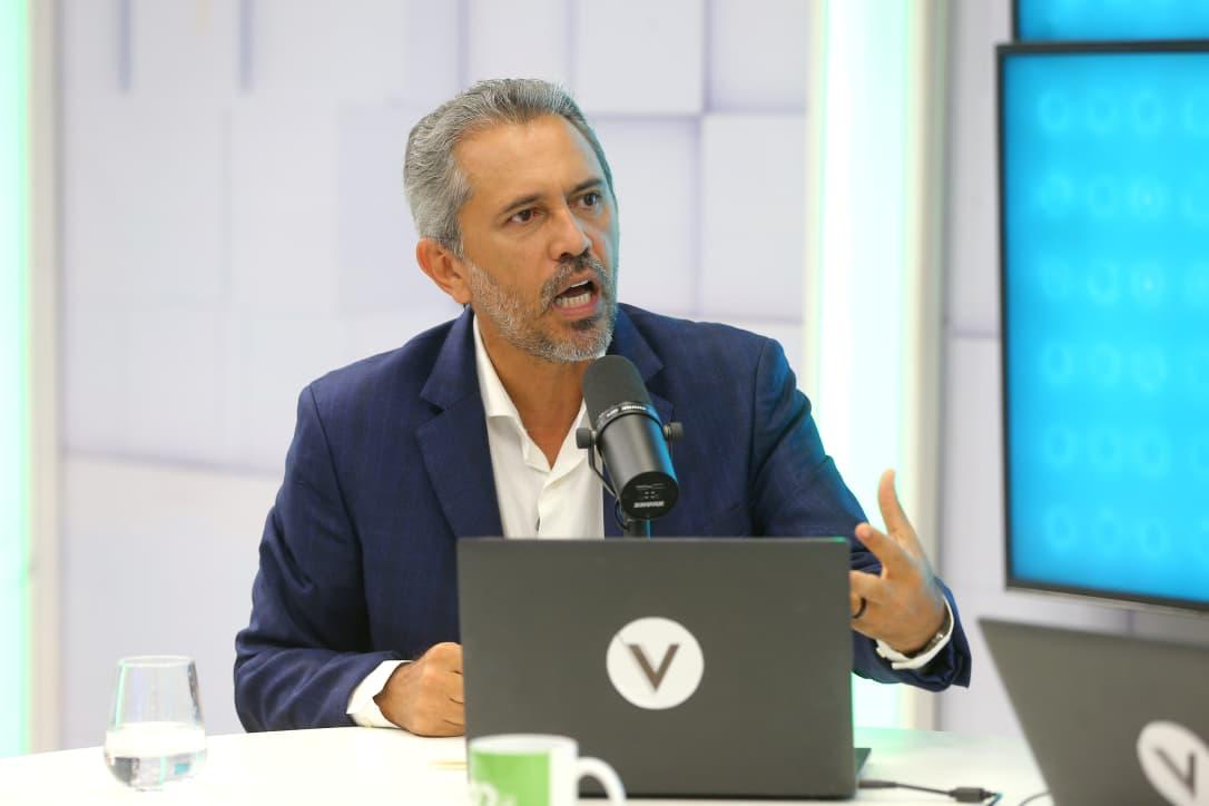 A imagem mostra o governador do Ceará Elmano de Freitas, sentado, gesticulando com as mãos em cima da mesa, durante entrevista, em um estúdio do Sistema Verdes Mares.