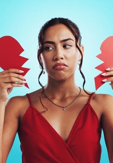 Mulher segura coração partido. Ela está com a expressão triste.