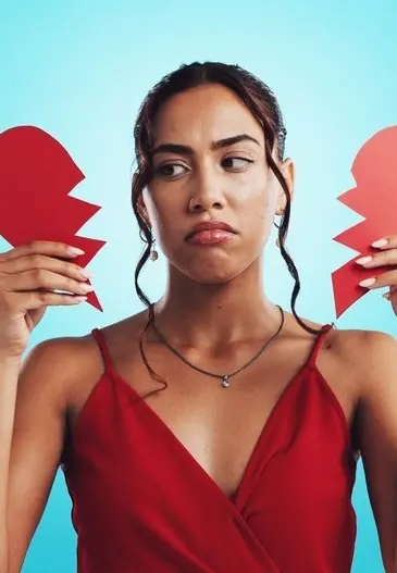 Mulher segura coração partido. Ela está com a expressão triste.