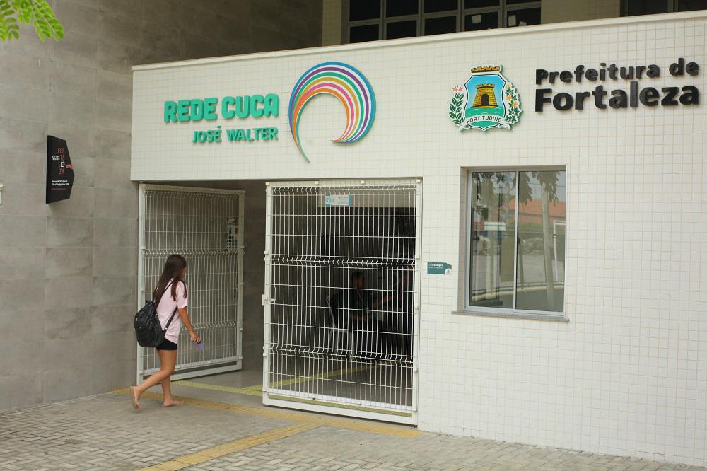 Entrada do Rede CUCA José Walter com jovem caminhando em direção ao portão.