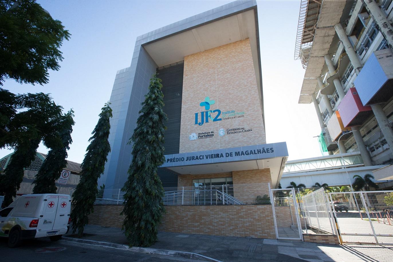 Fachada do Prédio Juraci Vieira de Magalhães do IJF2, em Fortaleza, Ceará, com arquitetura moderna, logos institucionais e uma ambulância estacionada na frente.