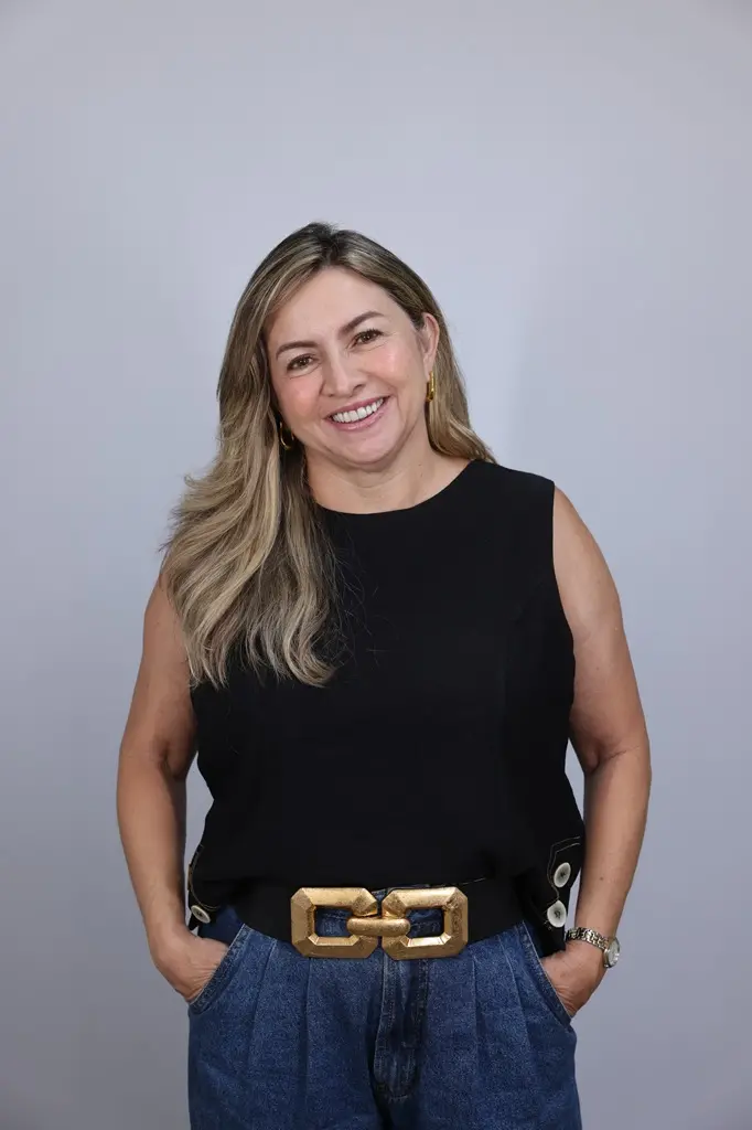 Ana Quezado, com camisa preta e calça jeans, posa para a foto com as mãos nos bolsos.