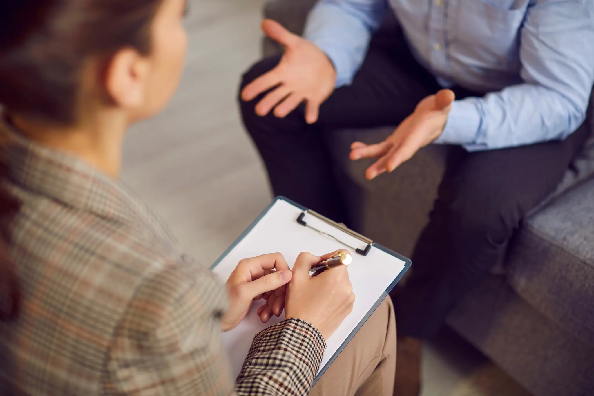 Paciente gesticula enquanto fala durante sessão com psicóloga, que o observa e faz anotações em um papel.