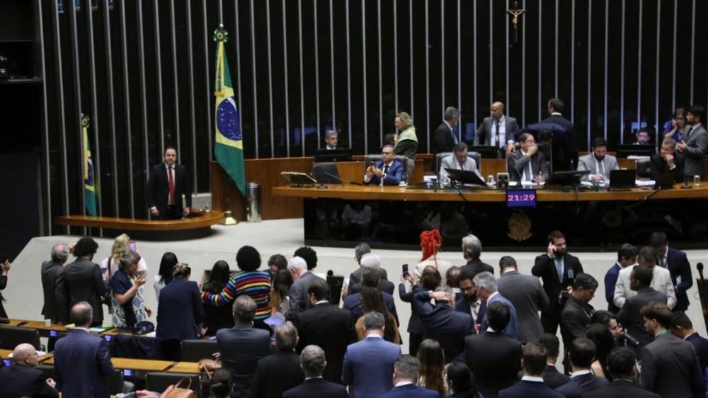 Plenário da Câmara dos Deputados com parlamentares sentados e em pé discursando.