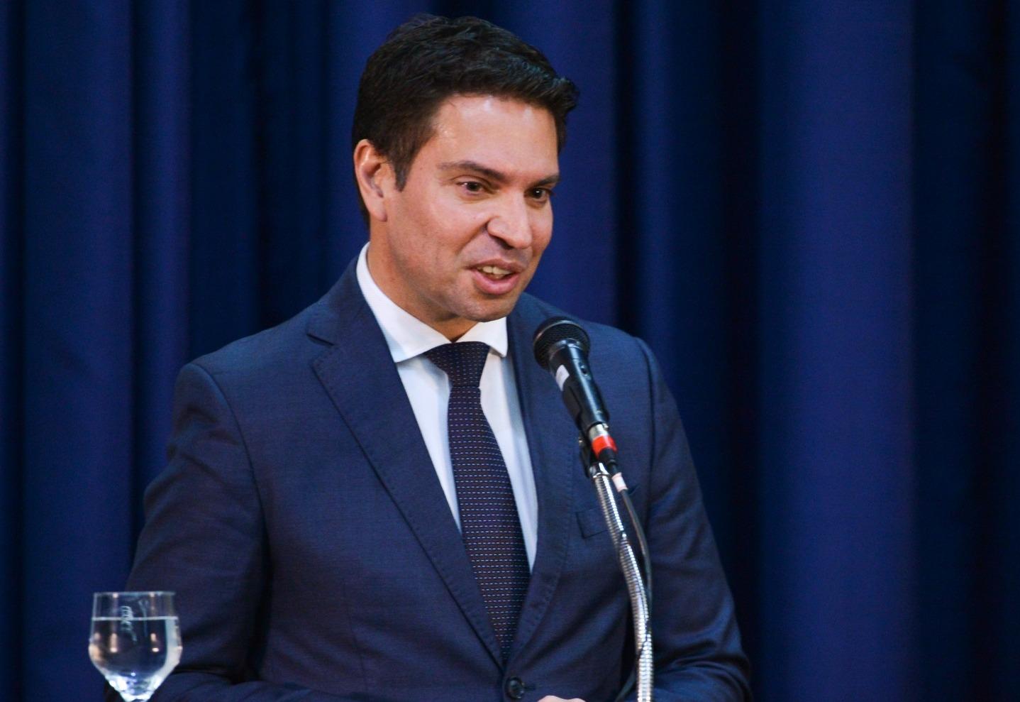 Alexandre Ramagem é um homem de meia idade, branco e de cabelo preto curto. Na foto, usa terno azul, camisa social branca e gravata azul.