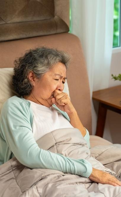 Idosa tossindo deitada na cama.