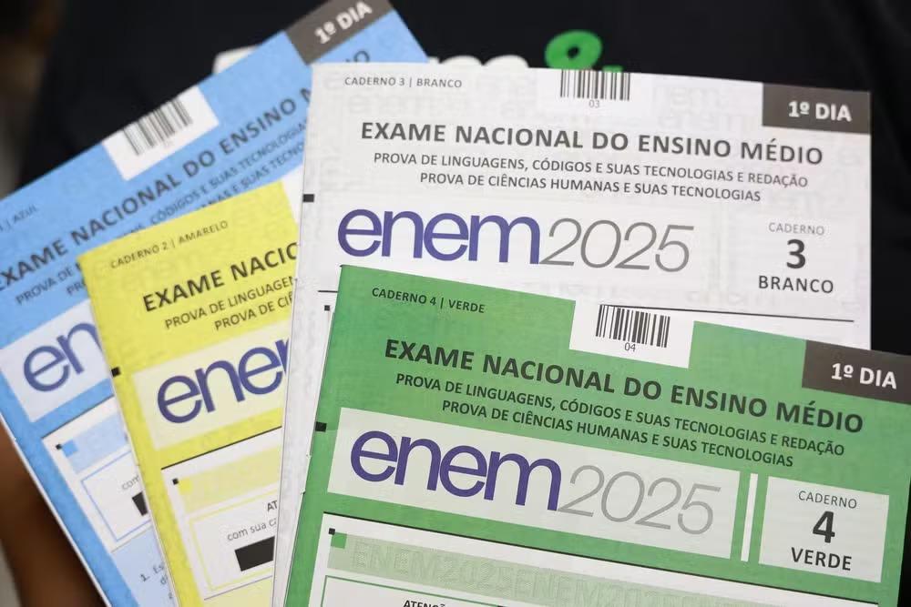 Visão detalhada de múltiplos cadernos de prova coloridos do ENEM 2025, destacando o '1º DIA' e as matérias de Linguagens, Códigos e Redação, e Ciências Humanas.