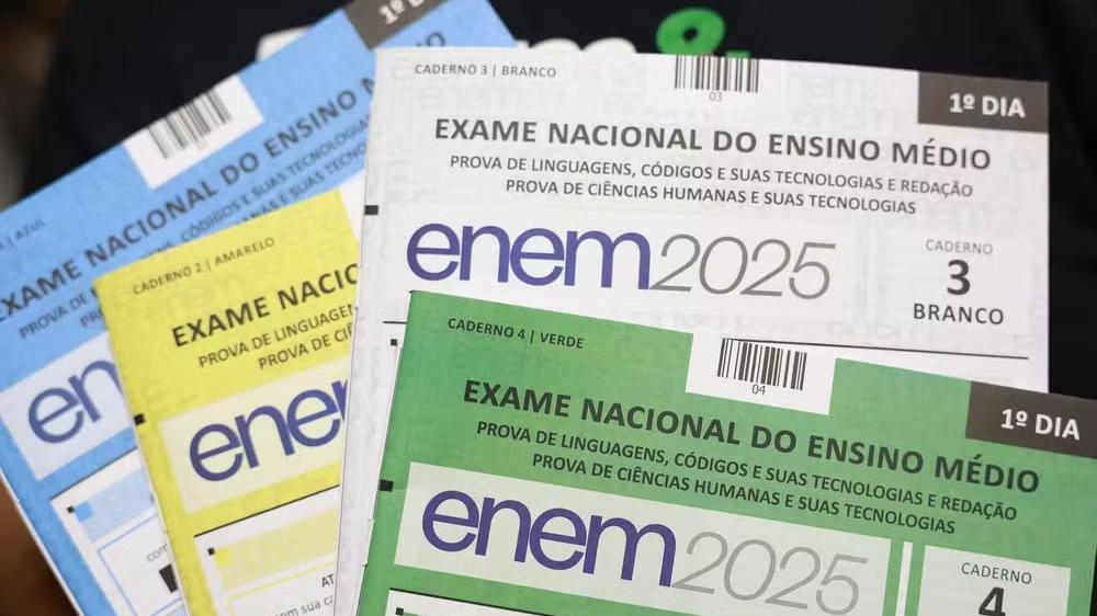 Visão detalhada de múltiplos cadernos de prova coloridos do ENEM 2025, destacando o '1º DIA' e as matérias de Linguagens, Códigos e Redação, e Ciências Humanas.